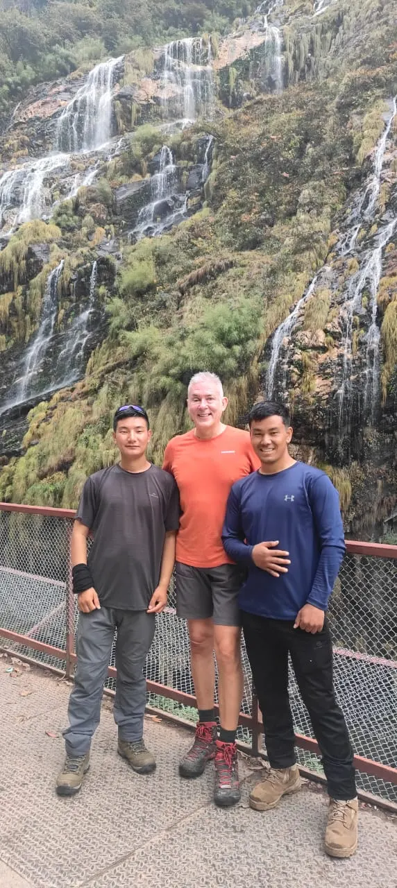 Three trekkers standing in front of a tall waterfall