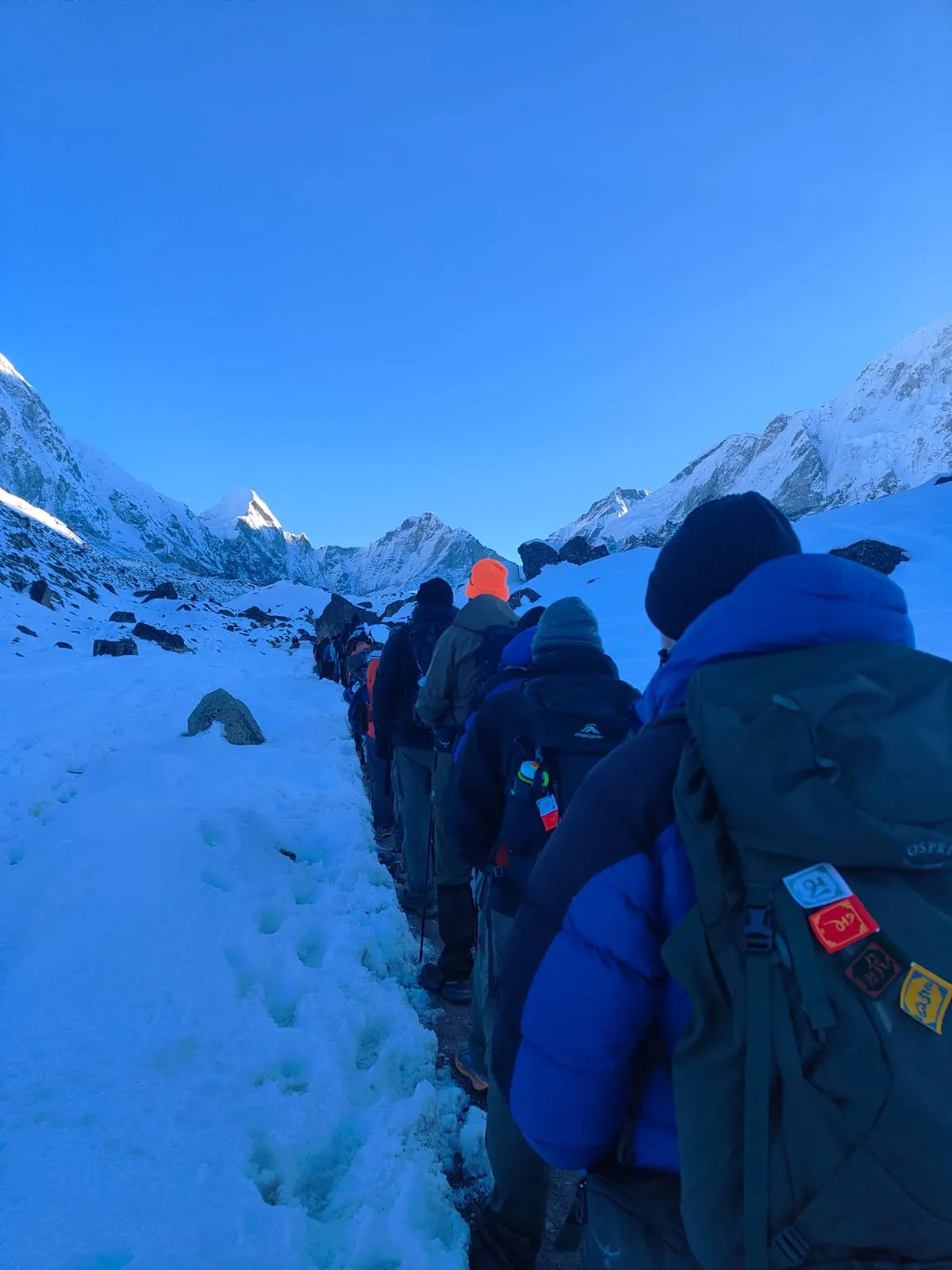 A line of trekkers in down jackets walking along a snow-covered path