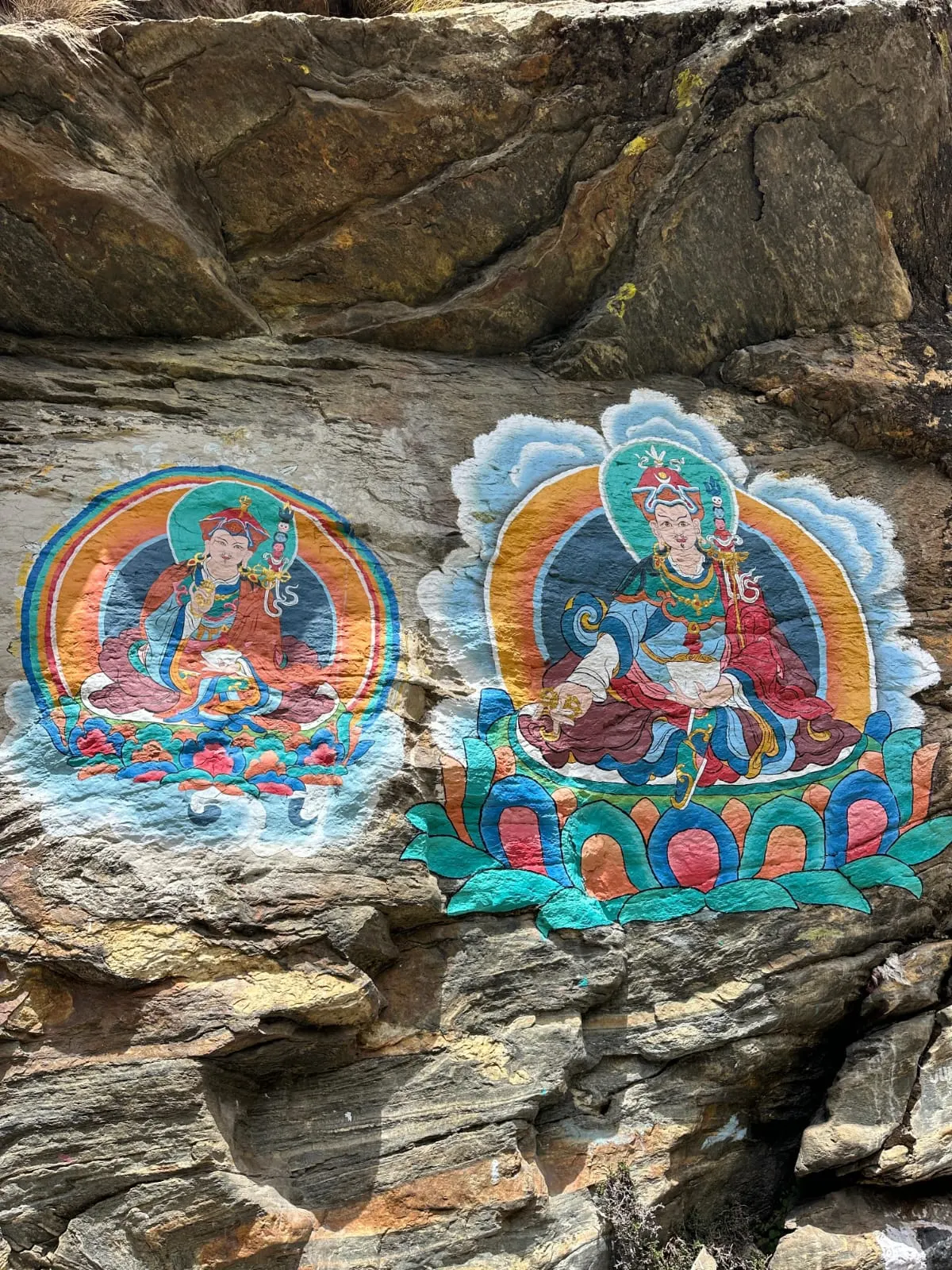 Colourful Buddhist figures painted on a rock face beside the trail