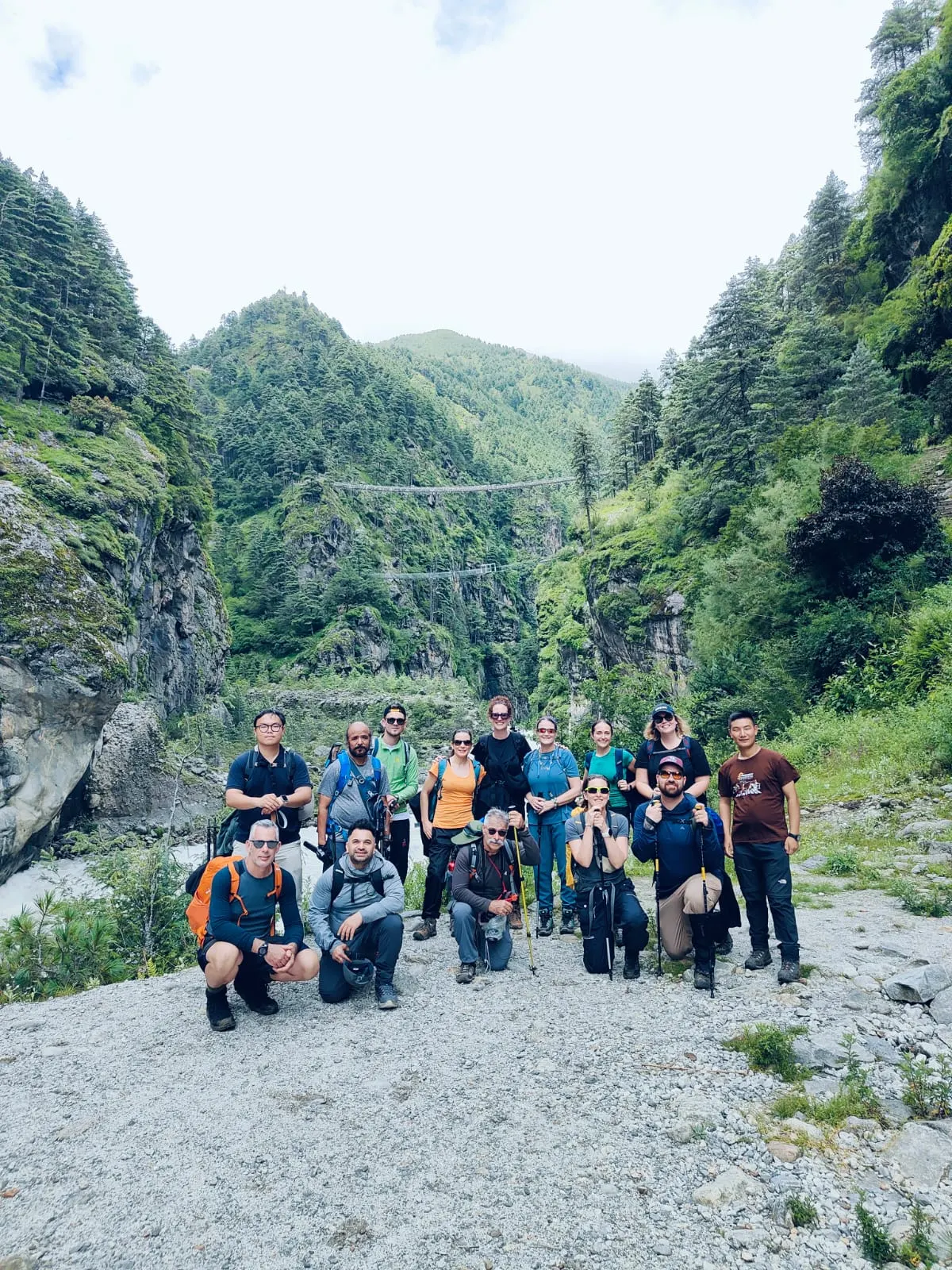 A trekking group posing on a riverbed in a green, misty valley