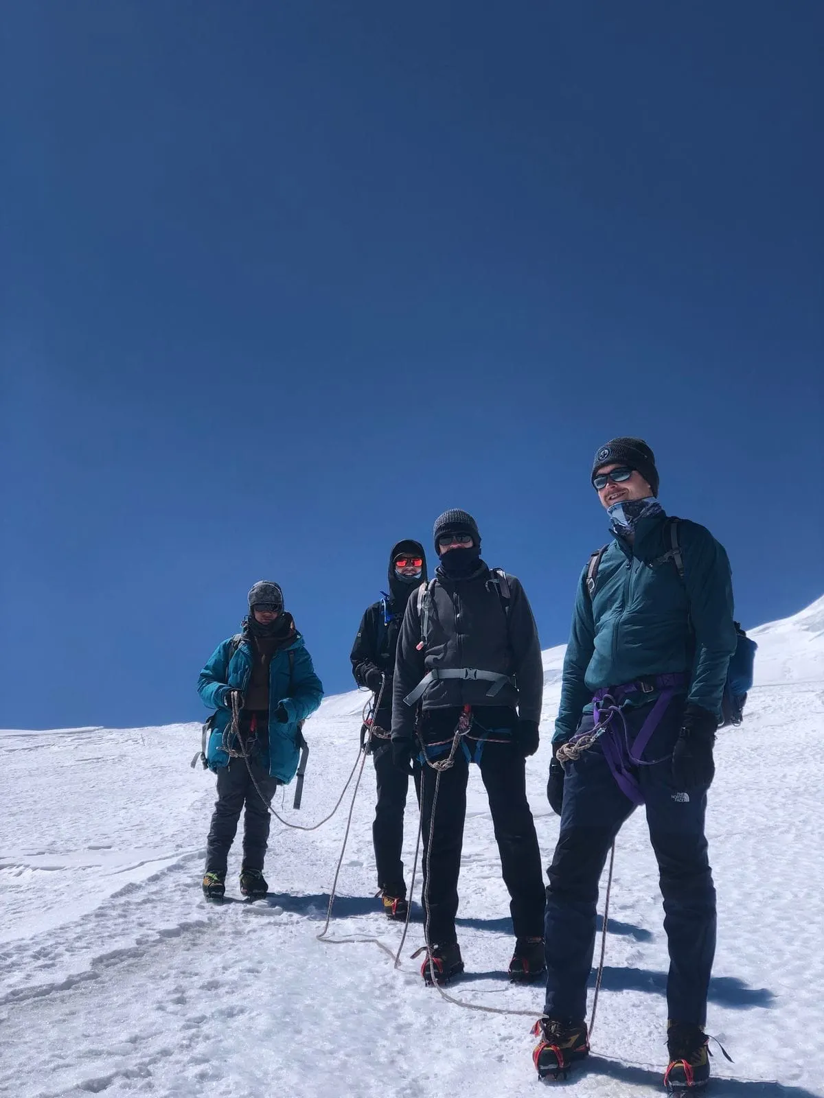 Four roped climbers in harnesses walking across a snowfield
