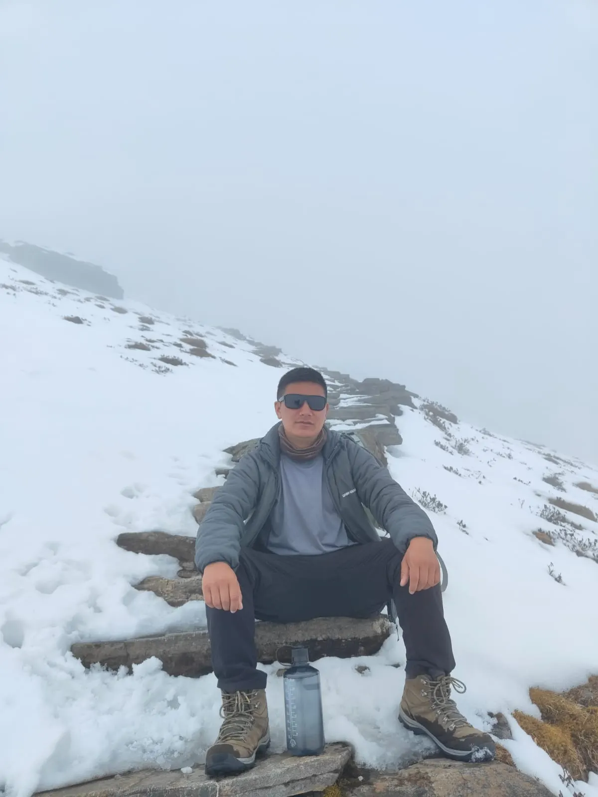 A man sitting on a stone step on a snowy, misty hillside