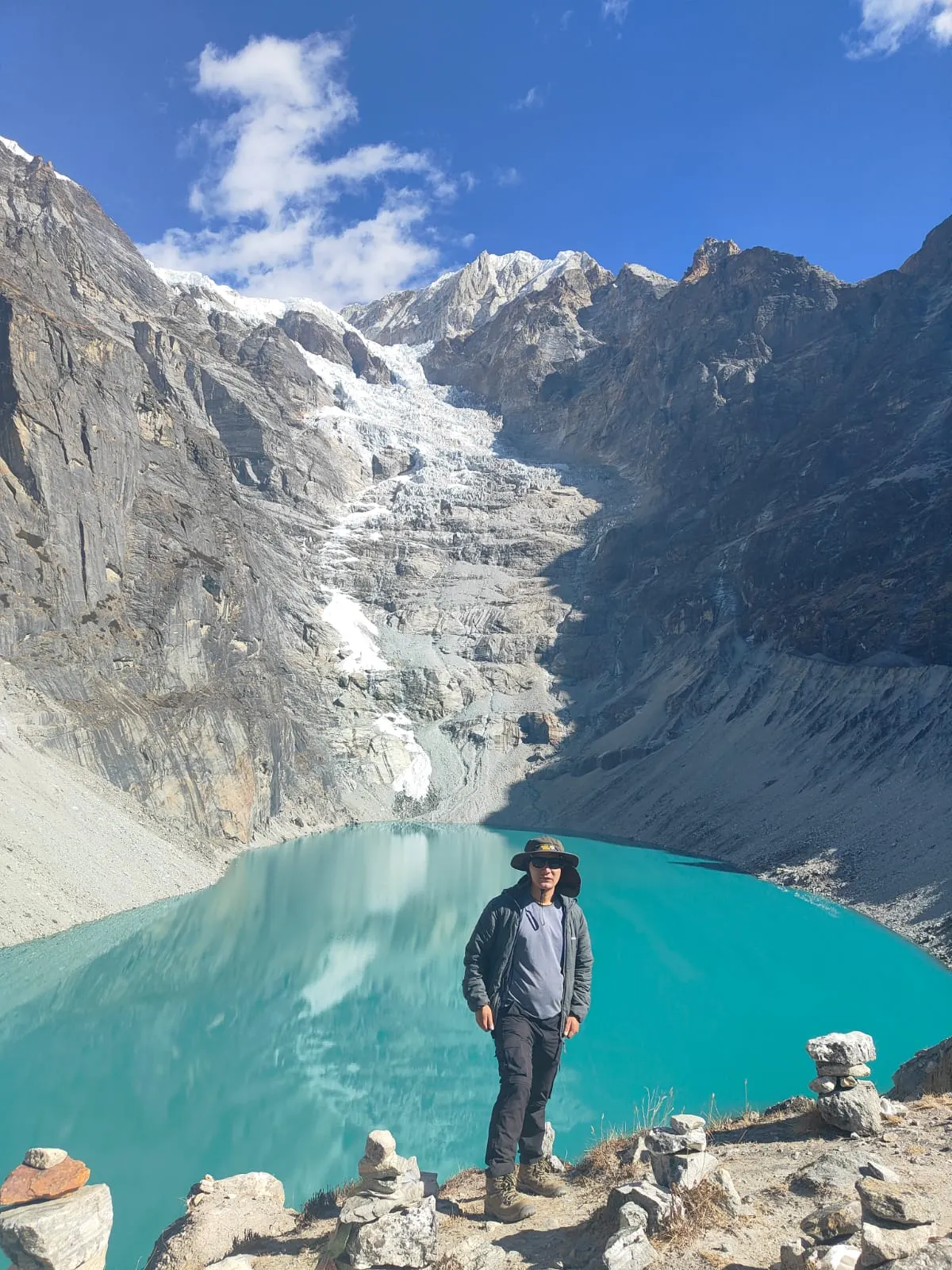 A trekker standing beside a turquoise glacial lake below a glacier
