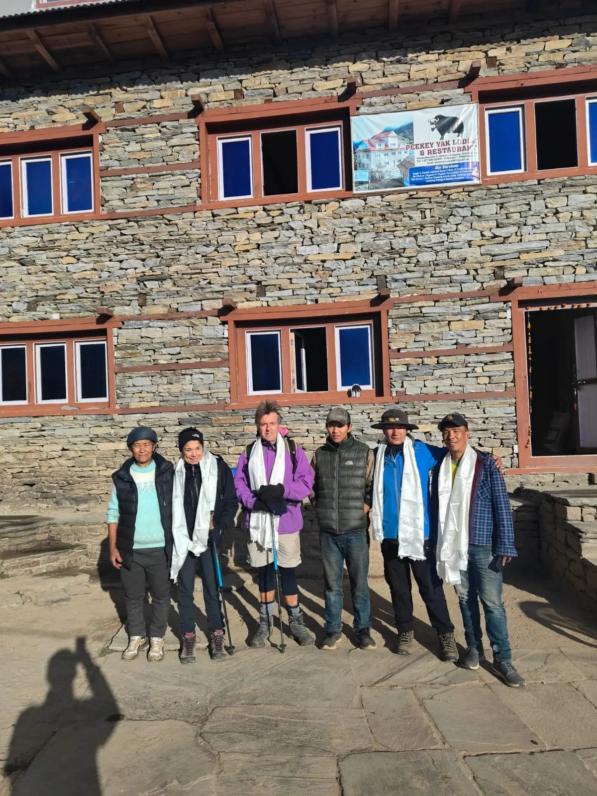 A group of trekkers wearing white scarves in front of a stone lodge