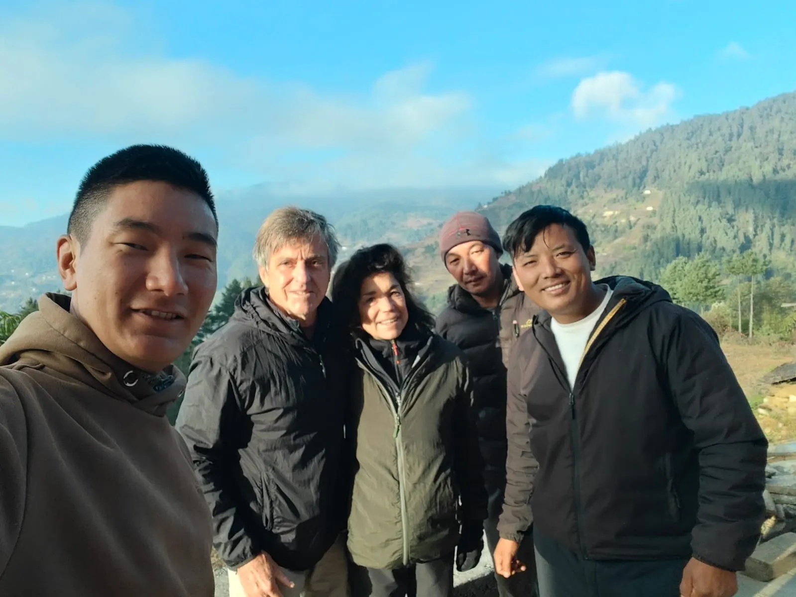 A smiling group selfie with forested hills behind