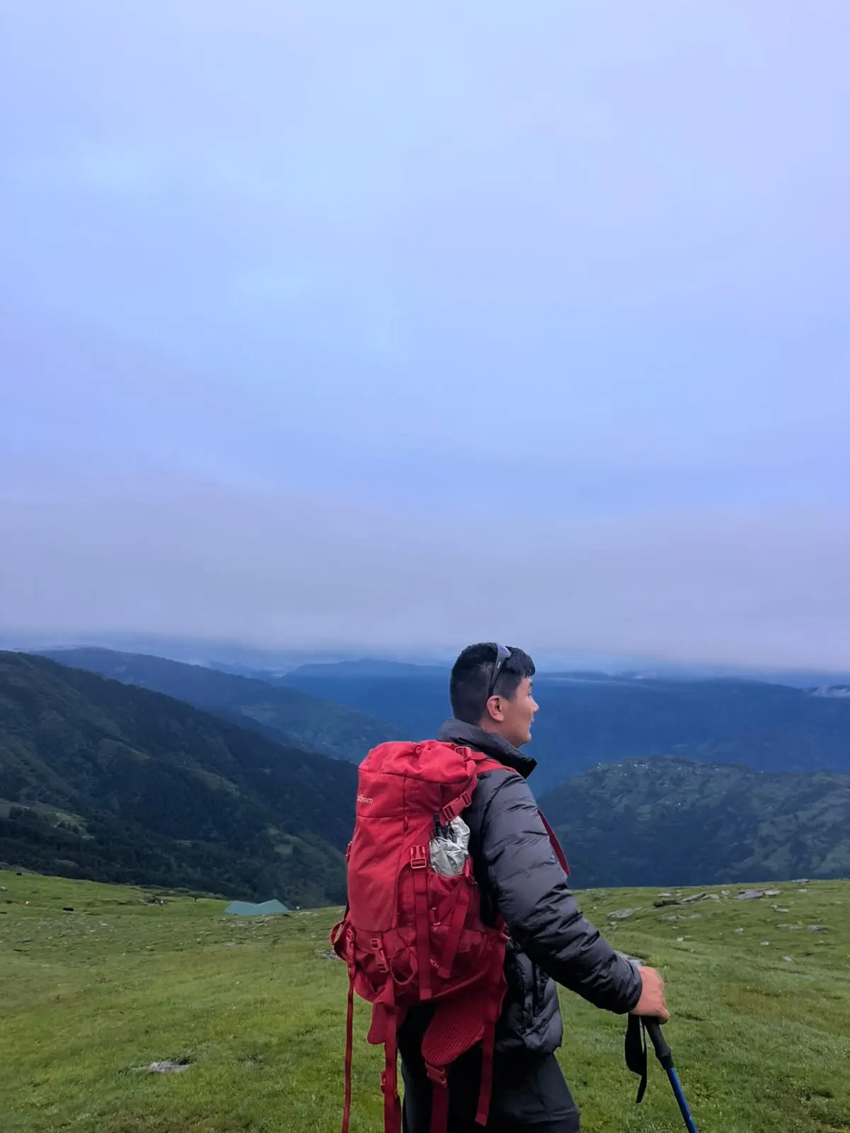 A trekker with a red backpack looking across green hills in the early light